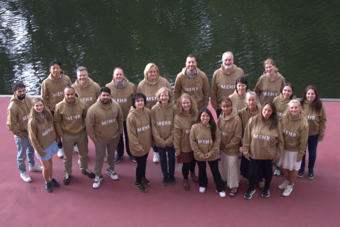 Gruppenfoto von Mitarbeitern bei CPP mit braunen Hoodies am Wasser.