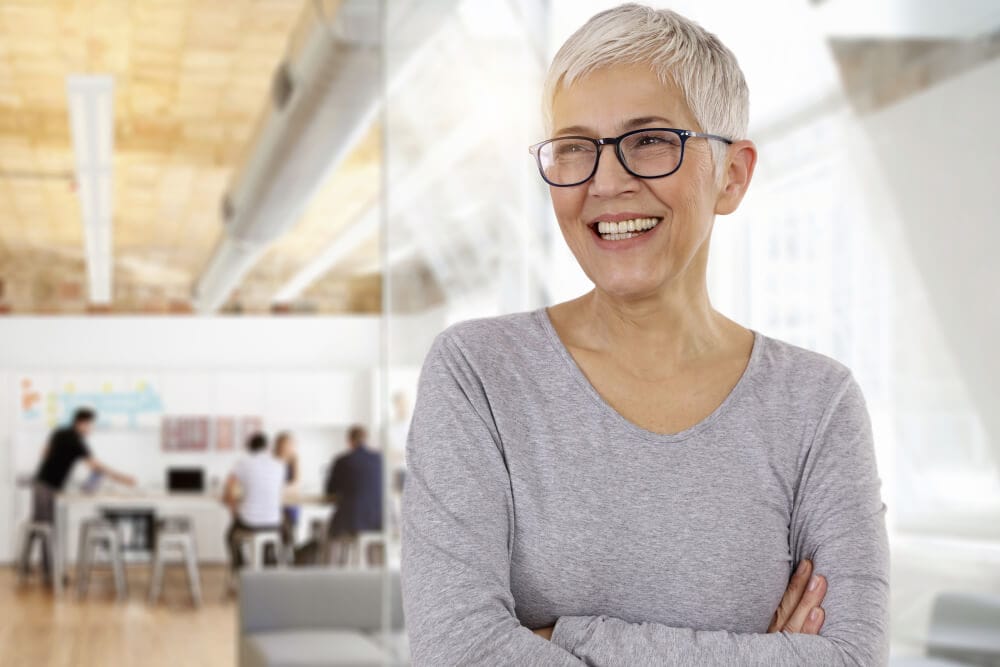 Erfahrene Lohnbuchhalterin im modernen Büro mit Team im Hintergrund